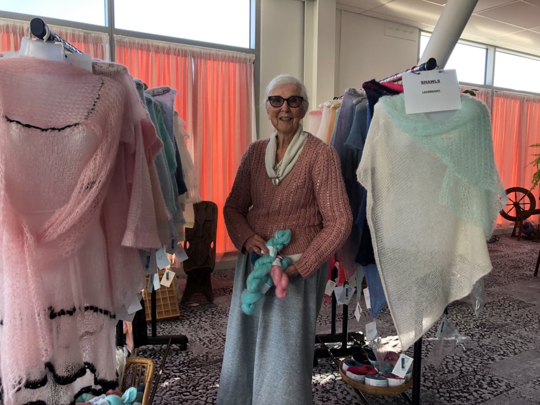 Margaret Richardson holding some of  her hand dyed wool with her handmade shawls and knitwear on either side.