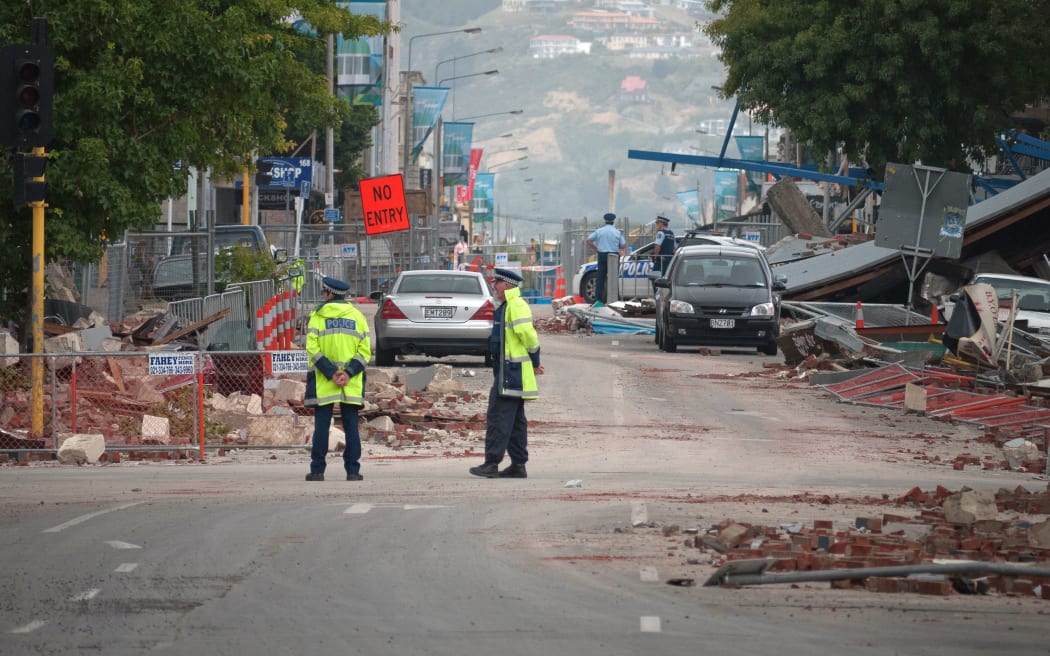 Police stand by amid fallen debris in a cordoned-off street in the aftermath of the Christchurch earthquake.