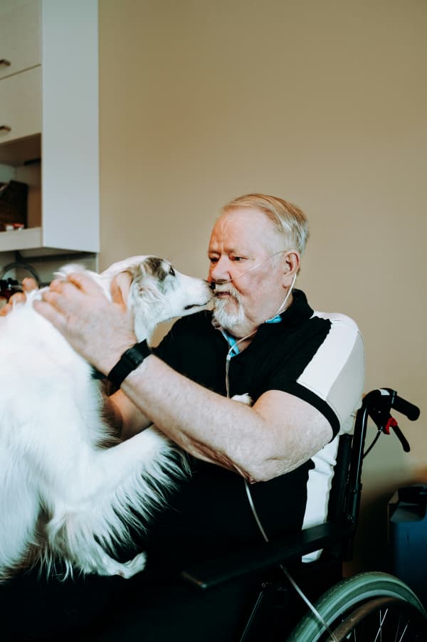 A man in a wheelchair embraces a white dog.