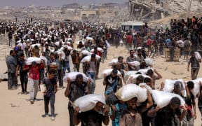 People walk with sacks of flour delivered after trucks carrying humanitarian aid entered northern Gaza on 27 July, 2025 coming from the Zikim border crossing.