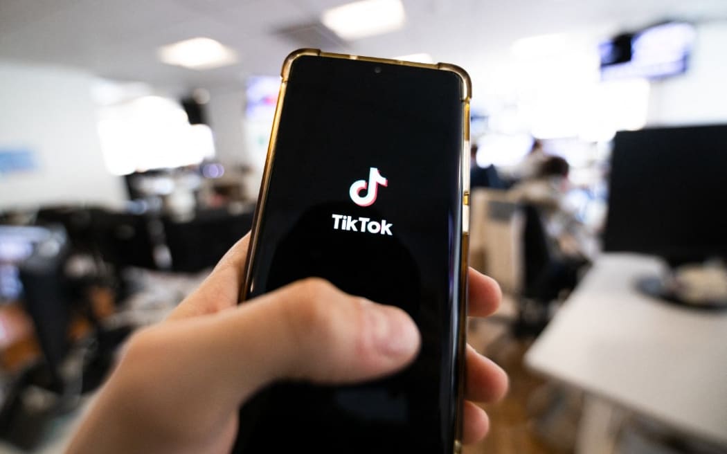 This photograph taken on April 19, 2024 shows a man holding a smartphone displaying the logo of Chinese social media platform Tiktok in an office in Paris (Photo by Antonin UTZ / AFP)