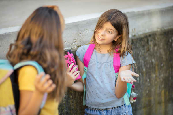 Two schoolgirls wearing backpacks and chatting after school.