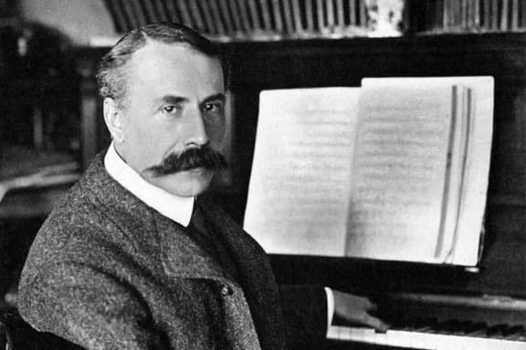 Composer Edward Elgar, seated at a piano, looking towards us, around 1900.