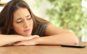 Sad girl waiting for a phone call and looking at device at home