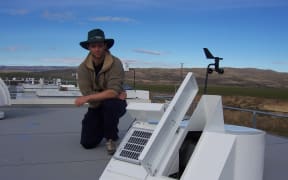 Dan Smale on top of the NIWA's Lauder atmospheric research laboratory building kneeling behind a solar tracker that feeds light into a Fourier transform spectrometer used to measure atmospheric trace gases.