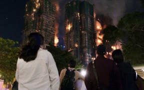 People look on as thick smoke and flames rise during a major fire at the Wang Fuk Court residential estate in Hong Kong's Tai Po district on 26 November, 2025.