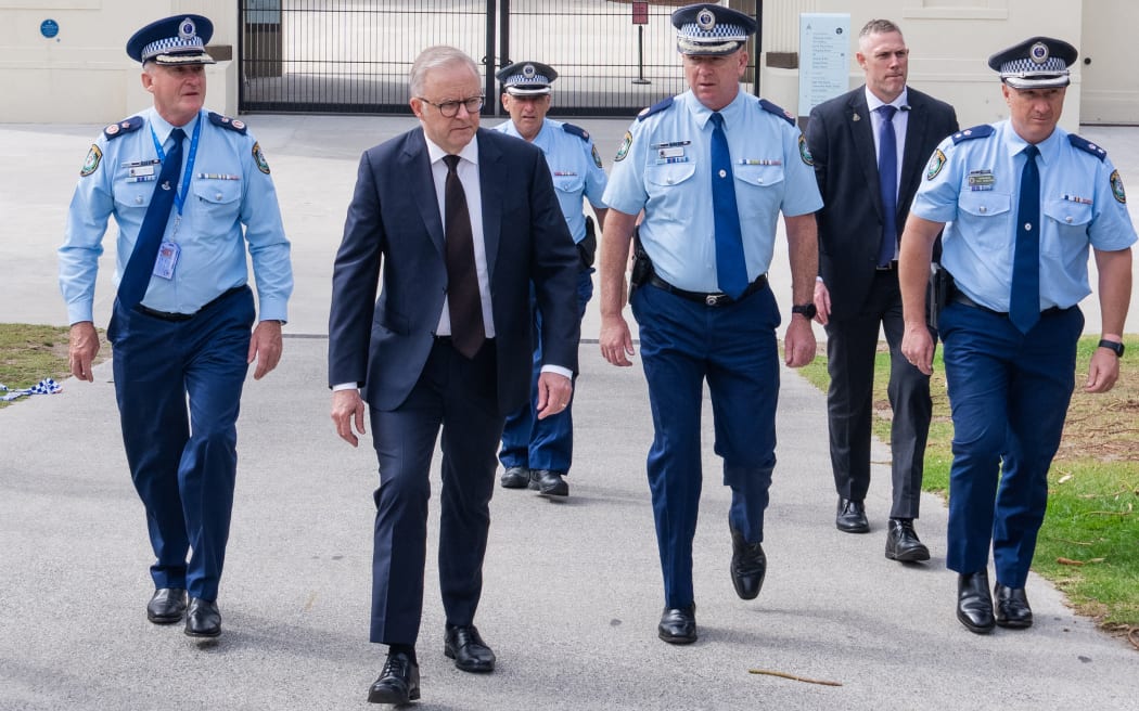 A handout photo taken and released by the Australian Prime Minister's Office on December 15, 2025 shows Australia's Prime Minister Anthony Albanese (2nd L) walking with police officers after laying flowers at the Bondi Pavilion at Bondi Beach, the scene of a shooting where 15 people were killed. A father-and-son team toting long-barrelled guns shot and killed 15 people including a 10-year-old girl at Sydney's Bondi Beach on December 14, with authorities labelling it an antisemitic terrorist attack on a Jewish festival.