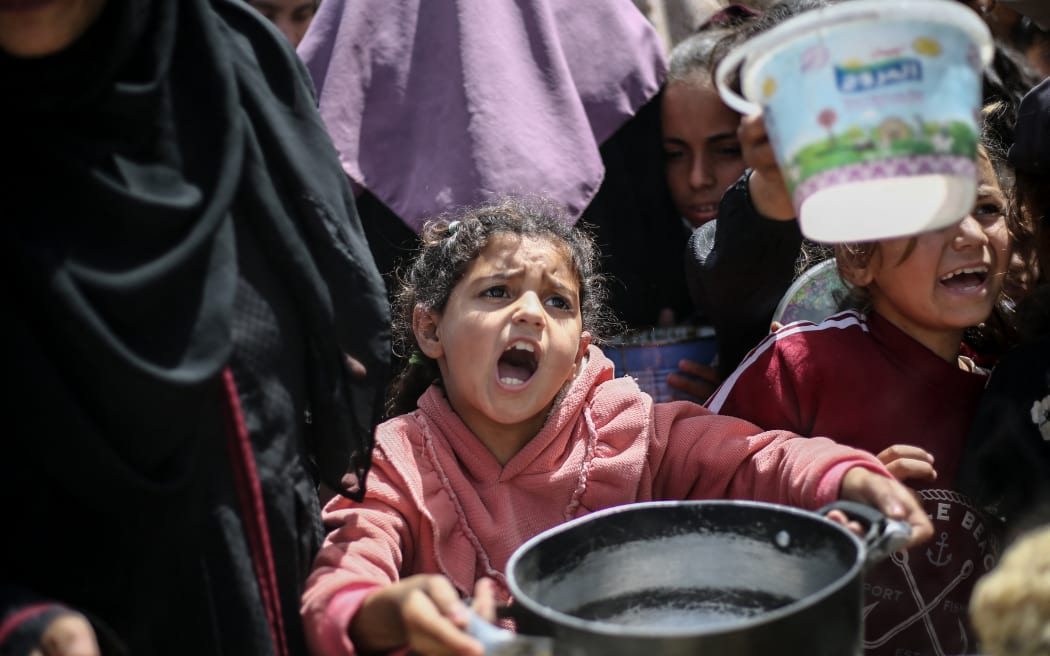 A girl gestures as Palestinian children line up to collect a meal at a free food distribution point in the Nuseirat refugee camp in the central Gaza Strip, on 3 April, 2025.