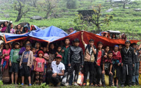Nepalese villagers shelter from rain under foam and plastic sheets at they wait for aid