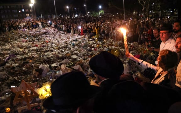 A candle is held up ahead of the seventh candle being lit for the  Jewish festival of Hanukkah as mourners stand next to floral tributes laid out in memory of the victims of a shooting at Bondi Beach, in Sydney, on 20 December, 2025.