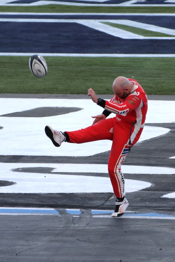 Shane Van Gisbergen kicks a rugby ball into the stands after winning a NASCAR race in 2025.