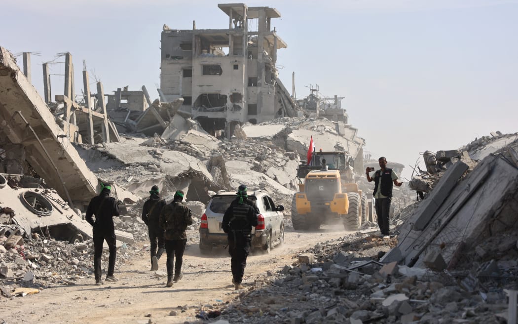 Armed Palestinian Hamas militants along with members of the International Red Cross (ICRC) follow a digger which has been supplied by Egypt, as a search for the bodies of killed Israeli hostages takes place, in Gaza City on November 2, 2025. Despite occasional flare-ups, a fragile truce has been holding in Gaza since October 10, 2025, based on a US-brokered deal centred on the return of all Israeli hostages, both living and dead. Israel has accused Hamas of not returning the dead hostages quickly enough, but the Palestinian group says it will take time to locate remains buried in Gaza's ruins. (Photo by Omar AL-QATTAA / AFP)