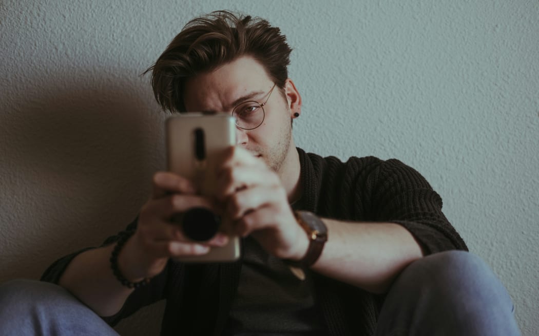 A young man squints at his phone.