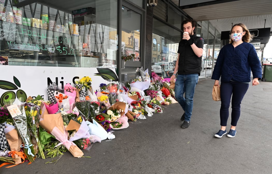 People walk past a floral tribute to a popular Melbourne delicatessen owner who died from Covid-19, 11 October 2021.