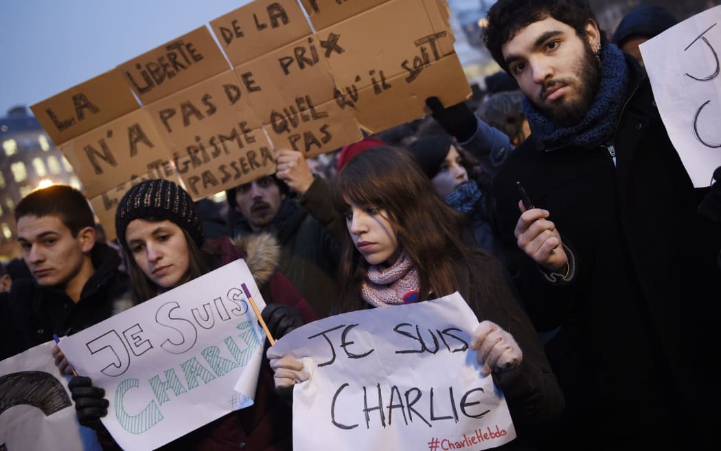 A man holds a placard reading: "Freedom of the press is priceless, fundamentalism, of any kind, will not pass" as others hold up pens and placards reading in French, "I am Charlie" during a gathering at the Place de la Republique in Paris.
