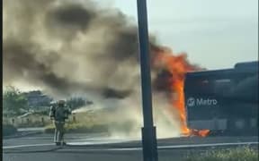 A firefighter uses a water hose to douse flames on an Auckland Transport Metro bus.