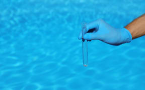 Man holding test tube with water against swimming pool on sunny day.