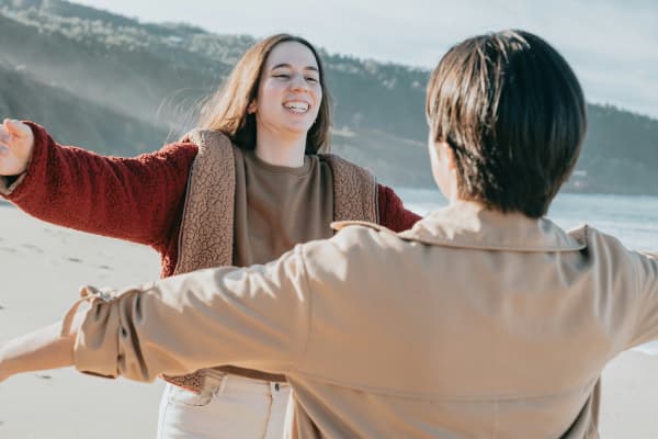 Two people with arms wide open, going for a hug, on a beach.