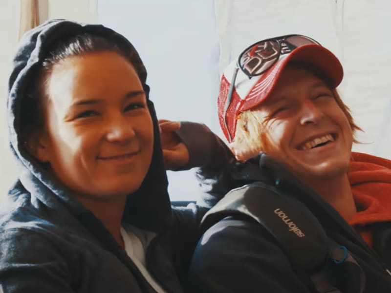Two smiling young people - a woman wears a hoodie and man wears a trucker cap.