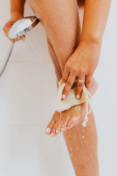 A woman cleans her foot with a cloth in the shower