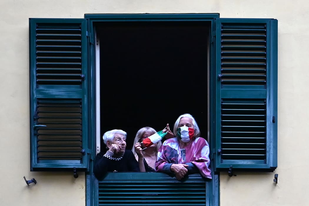 People with protective masks look from their windows at artists performing for the show Sotto lo Stesso Cielo tour (Under the Same Sky tour) in Rome on 18 April 2020.