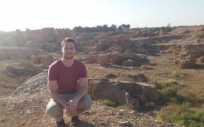 Paul Cooper crouches next to the ruins of Babylon, Iraq, which are overlooked by one of Saddam Hussein's abandoned palaces.