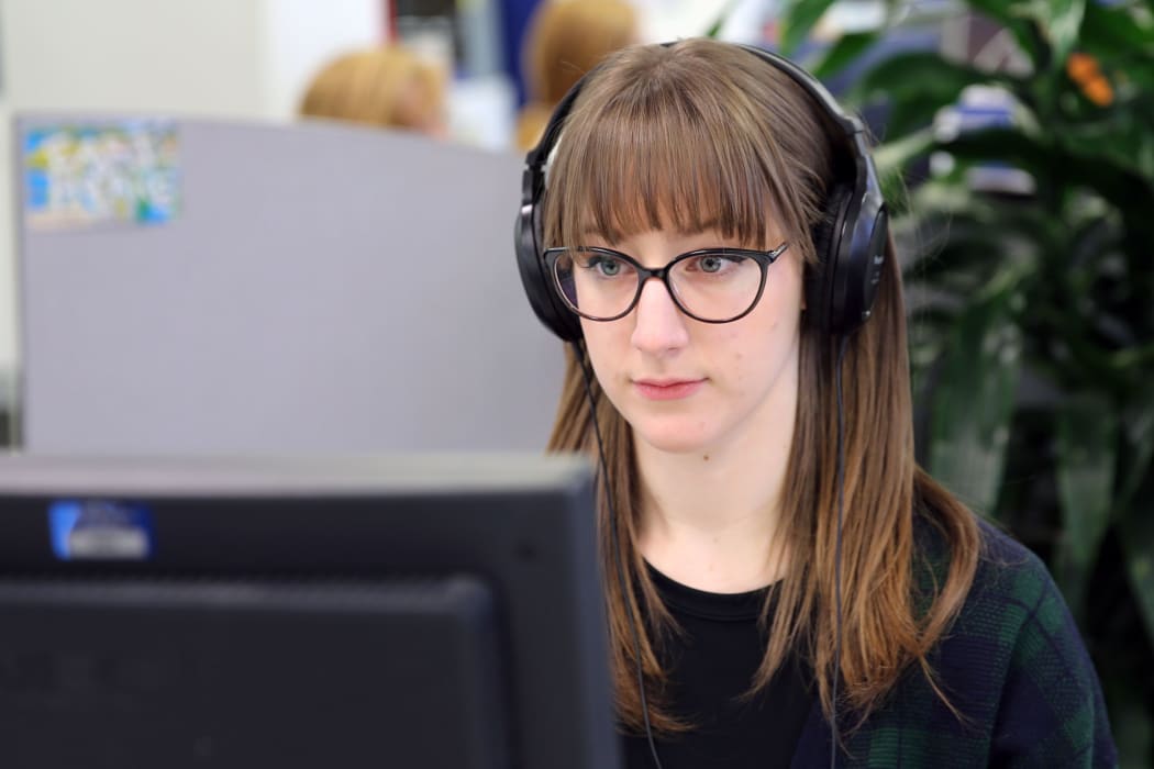 A picture of Louise Burston at work at a computer wearing headphones