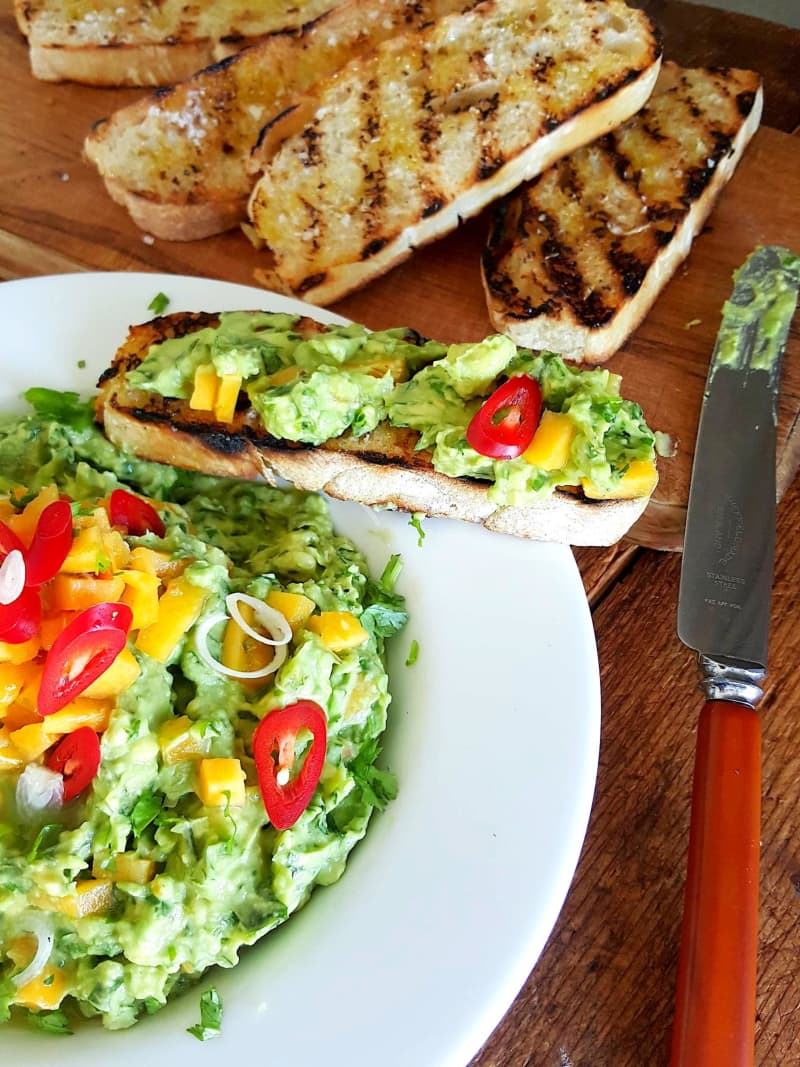 A dish of peach and avocado guacamole, garnished with toasted bread and finely chopped chilli and spring onion.