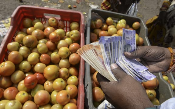 A trader counts money at a vegetable wholesale market in Hyderabad on 24 November 2021, as the retail price for tomatoes reached rupees 100 per kg due to unseasonal rains and a hike in fuel cost in several parts of the country.