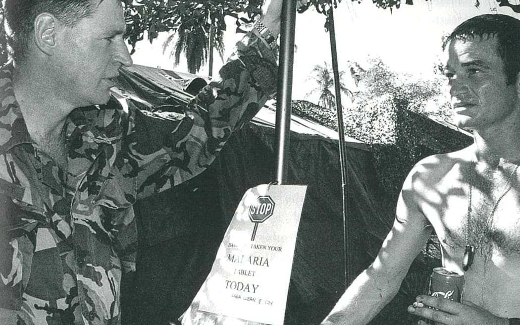 : Lieutenant Colonel Kevin Burnett (at left) talking to one of his men. The sign in the middle of the photograph reminds personnel to take their daily doxycycline tablet to guard against malaria.