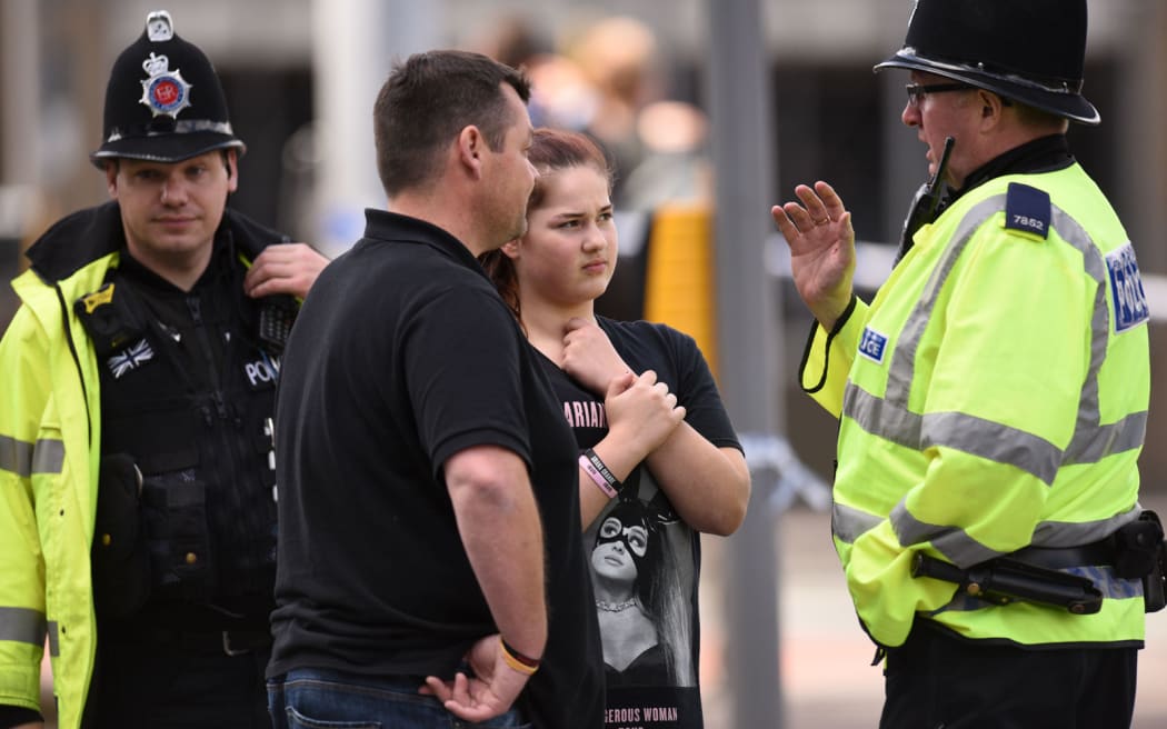 A police officer talks to a man and girl wearing an Ariana Grande t-shirt outside Manchester Arena.