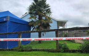 Police are executing a search warrant at a house on Taraire Street in relation to the investigation into the homicide of Linda Woods. At least four officers are guarding the cordoned house and other officers can be seen rummaging through rubbish bins on the property.