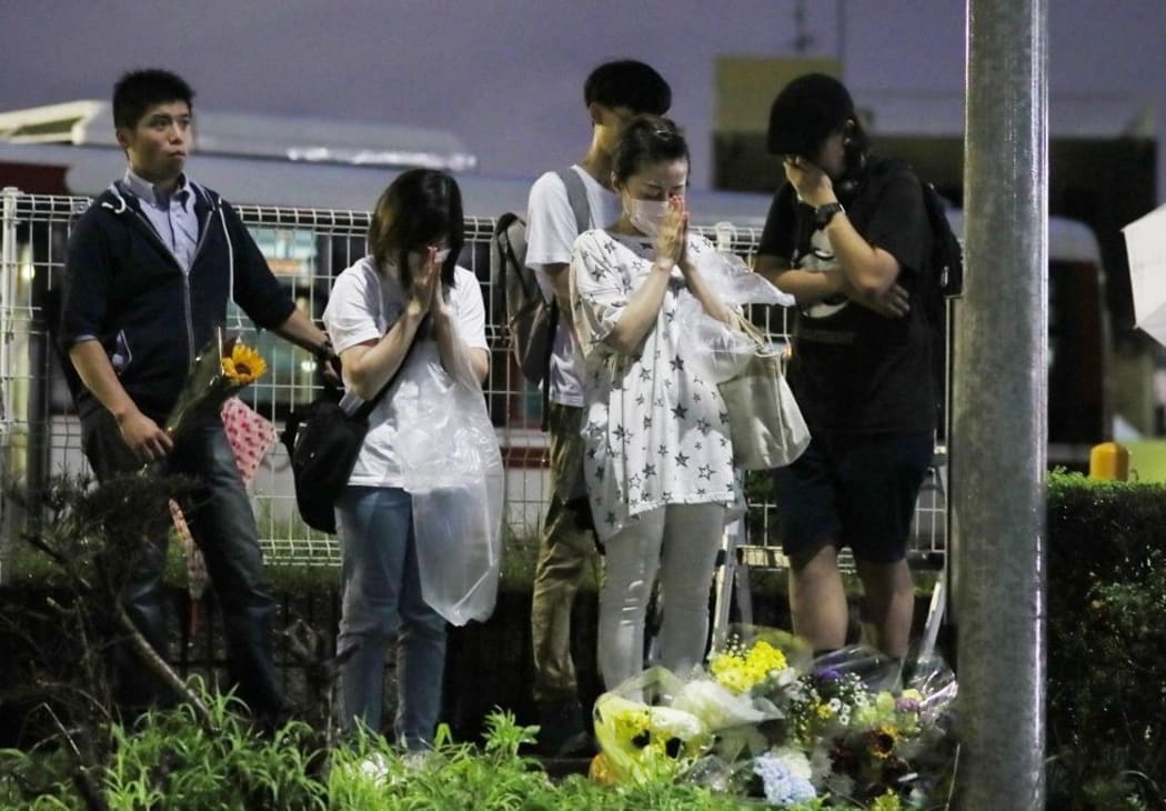 People place their hands together towards the fire site at Kyoto Animation Co., Ltd. (so-called Kyoani) in Kyoto on July 19, 2019, one day after the arson.