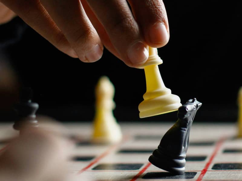 A close-up of a hand knocking down one chess piece with another.