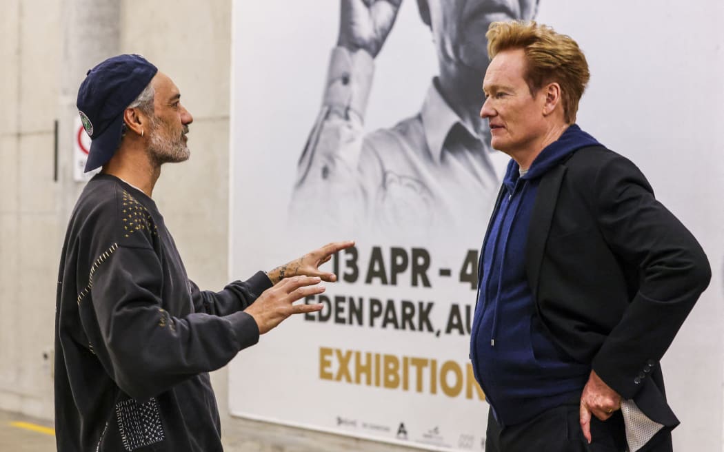 New Zealand filmmaker-actor Taika Waititi (L) and US comedian and television personality Conan O’Brien interact ahead of a world record attempt for the largest mass Haka, at Eden Park in Auckland on September 29, 2024. Organisers hope a crowd of up to 10,000 will smash the previous record, officially held by France since 2014, of the Maori war dance made famous by the All Blacks. (Photo by DJ Mills / AFP)