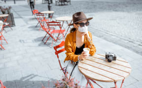 Young woman in facial mask sitting on the cafe terrace alone. Concept of social distancing and new social rules after coronavirus pandemic.