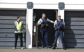 Two uniformed police and a person in a high vest vest with blue gloves stand outside a doorway.