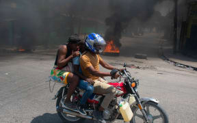 A woman with a child lowers her head as they leave the area on a motorcycle after gunshots were heard in Port-au-Prince, Haiti, on 20 March, 2024. Negotiations to form a transitional council to govern Haiti advanced on March 20, as the United States airlifted more citizens to safety from gang violence that has plunged the impoverished country into chaos. (Photo by Clarens SIFFROY / AFP)