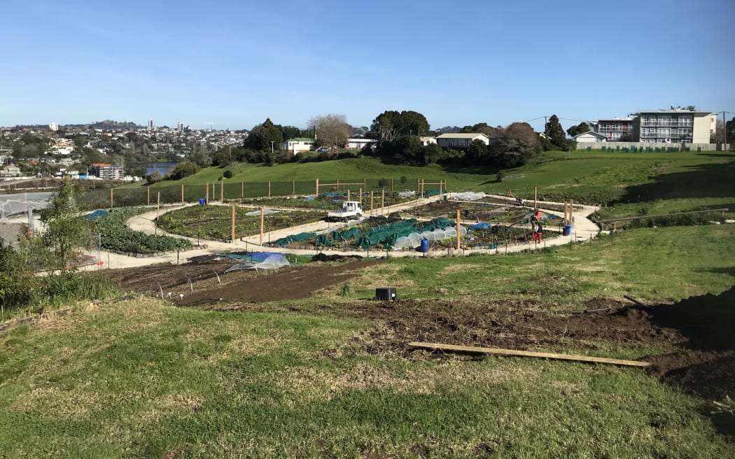 A large circular garden with a gravel path through it. There is a van parked on the path and some people are setting up grow tunnels.
