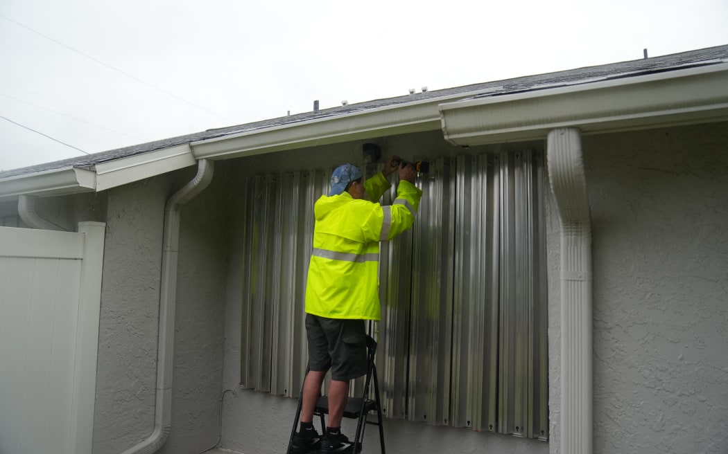 A resident secures aluminum shutters across windows in Dunedin ahead of Hurricane Milton's expected landfall tonight on October 9, 2024 in Florida. - Milton regained power on October 8 to become a Category 5 storm with maximum sustained winds of 165 mph (270 kph) as it barrels towards the west-central coast of Florida and is forecast to make landfall late October 9, according to the National Hurricane Center. (Photo by Bryan R. SMITH / AFP)