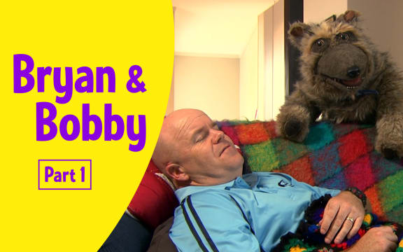 Photograph of Bryan (male adult) lying down on a couch with his eyes closed and Bobby (realistic large dog puppet) looking out towards viewer.
Text reads  "Bryan and Bobby Part 1”