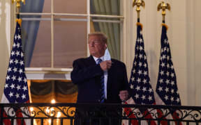 US President Donald Trump takes off his facemask as he arrives at the White House on 5 October, on his return from Walter Reed Medical Center, where he underwent treatment for Covid-19.
