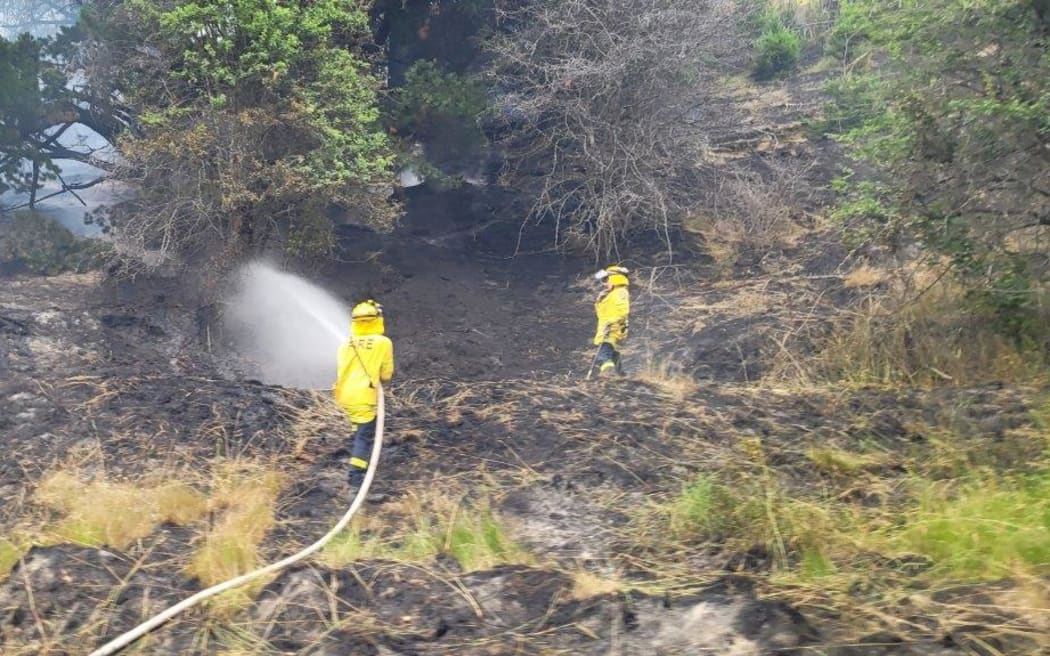 Firefighters hosing a vegetation fire at Long Gully near Coronet Peak on 20 January 2023.