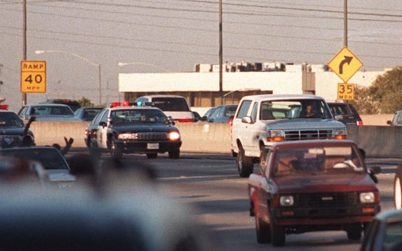 (FILES) Motorists wave as police cars pursue the Ford Bronco (white, R) carrying fugitive and murder suspect O.J Simpson on a 90 minutes chase on Los Angeles freeway on June 17, 1994. The car driven by Simpson's friend Al Cowling eventually drove to Simpson home in Brentwood where he surrendered after a stand-off with police. Simpson has died at the age of 76, his family said on April 11, 2024. (Photo by MIKE NELSON / AFP)