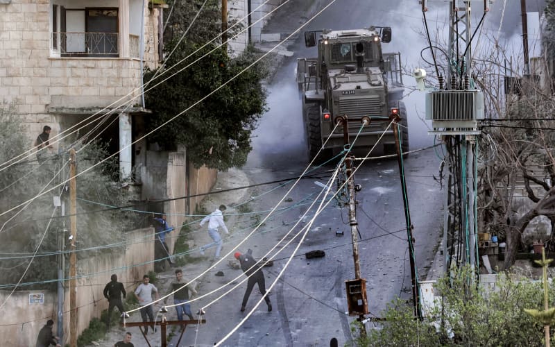 People confront an Israeli military vehicle during an Israeli army raid in the Jenin camp for Palestinian refugees in the occupied West Bank on March 7, 2023. Israeli troops killed six Palestinians.