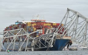 The steel frame of the Francis Scott Key Bridge sits on top of a container ship after the bridge collapsed, Baltimore, Maryland, on March 26, 2024. The bridge collapsed early March 26 after being struck by the Singapore-flagged Dali container ship, sending multiple vehicles and people plunging into the frigid harbor below. There was no immediate confirmation of the cause of the disaster, but Baltimore's Police Commissioner Richard Worley said there was "no indication" of terrorism.