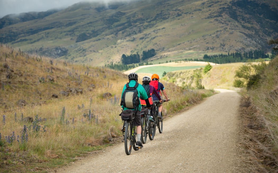 Three people cycling the Otago Central Rail Trail in a row towards Middlemarch, South Island, New Zealand.