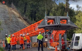 Workers watch on as a tower is put in place to hold the 1.1km cableway to take workers and materials to the site of the Mt Messenger bypass project, in North Taranaki.