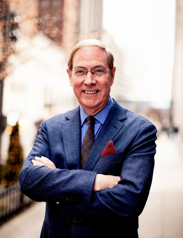 Gary Chapman is a smiling man in a blue suit and spectacles with his arms folded.