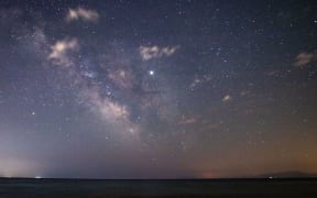 The Milky Way in Epanomi shipwreck beach near Thessaloniki in Greece. The water of the sea, Thermaikos Gulf, the shore of Epanomi and Kisavos mountain visible on the photo.